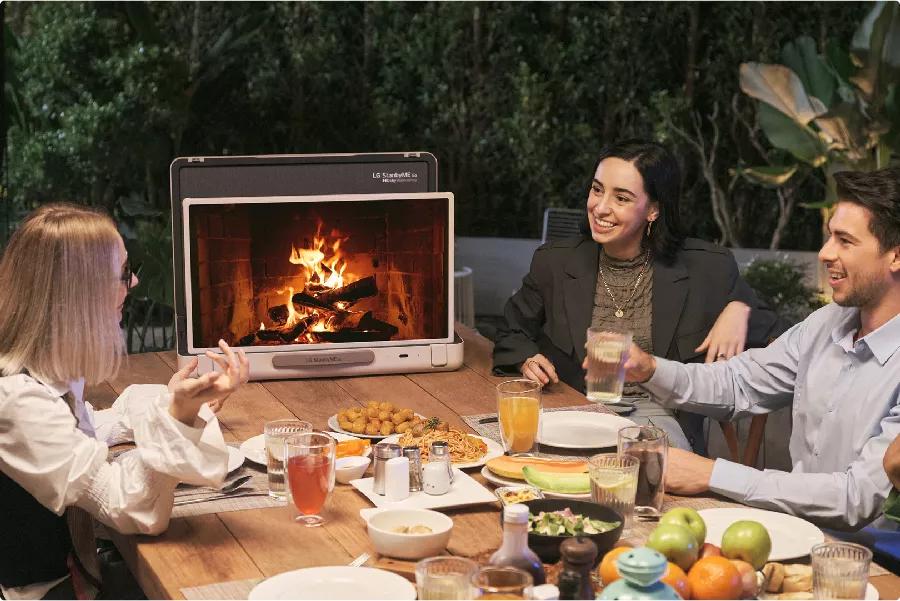מסך טאץ` חכם נייד GO StanbyME LG דגם 27LX5 A group of friends enjoys a meal with the TV displaying a fireplace on screen.